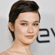 Cailee Spaeny stands in front of a wall with the Devs TV show's logo on it.